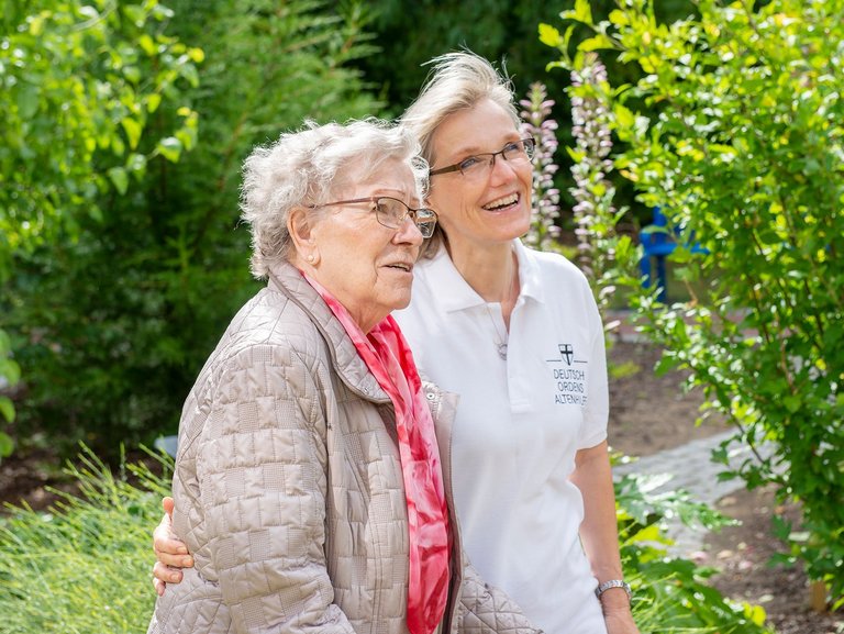 Im Garten: eine Pflegerin zeigt einer Bewohnerin etwas (nicht sichtbar)