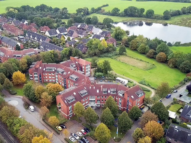 Luftbild: hauptsächlich rote Backsteingebäude - im Hintergrund ein Teich und Wiesen